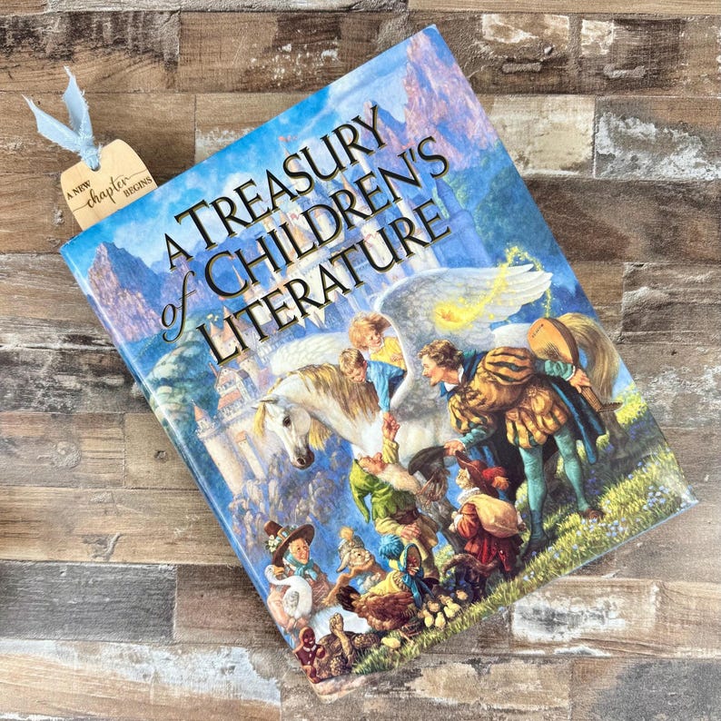 May include: A Treasury of Children's Literature book with a colorful illustration of a winged horse and figures. A light blue ribbon and a tag that reads "A New Chapter Begins" are attached to the book.