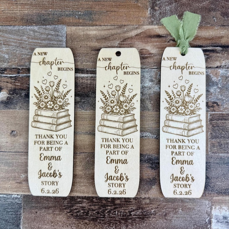 May include: Three wooden bookmarks with a floral and book design. The bookmarks have the text "A New Chapter Begins" and "Thank you for being a part of Emma & Jacob's Story 6.2.26". One bookmark has a green ribbon.