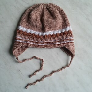 May include: A brown knitted hat with white and brown stripes and ear flaps. The hat has ties that can be tied under the chin.