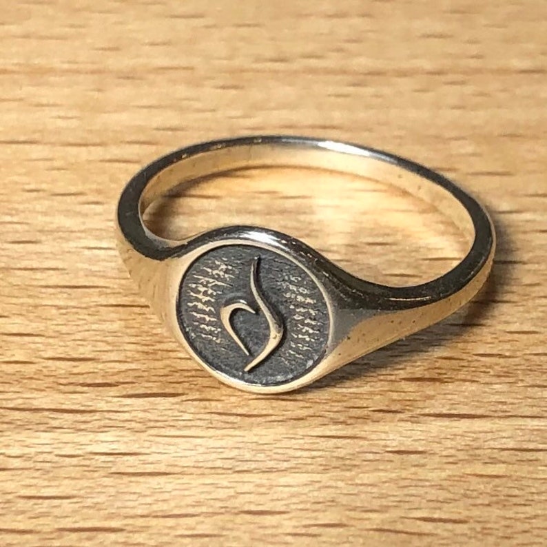 Puede incluir: Un anillo de plata con un dise&ntilde;o redondo y texturizado que presenta un s&iacute;mbolo estilizado. El s&iacute;mbolo es una 'S' estilizada.