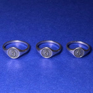 Puede incluir: Tres anillos de plata con un dise&ntilde;o de s&iacute;mbolo de infinito estilizado. Los anillos est&aacute;n sobre un fondo azul.
