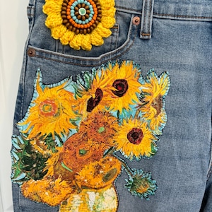 May include: Blue denim jeans with a yellow crochet sunflower applique on the pocket and a large patch of Van Gogh's "Sunflowers" painting on the leg. The sunflower applique has brown, orange, and blue beads in the center.