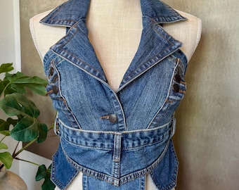 May include: A blue denim vest with a unique design, featuring a collar, button closures, and a belt detail. The vest is displayed on a mannequin, showcasing its tailored fit and style. The garment has a classic, timeless appeal.