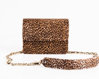 May include: A small brown and black leopard print handbag with a gold chain strap and a matching leopard print shoulder strap.