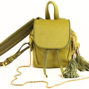 Könnte beinhalten: Ein kleiner grüner Rucksack aus Wildleder mit einer goldenen Kettenkette und zwei grünen Quasten.