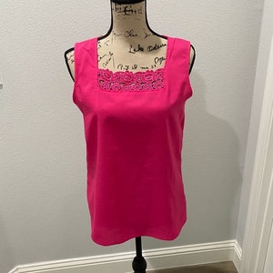May include: A sleeveless pink top with a square neckline and a lace trim. The top is on a white mannequin.