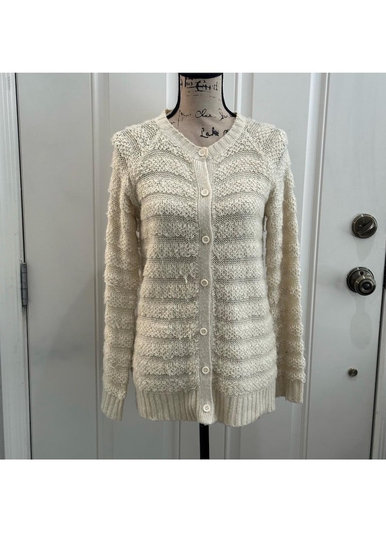 May include: A cream-colored knitted cardigan with a button-up front and a striped pattern.
