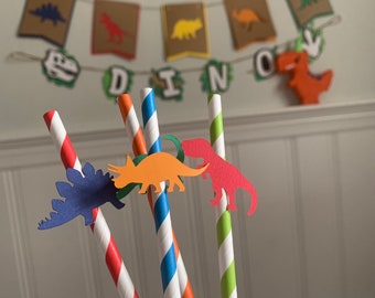 May include: Four striped paper straws with dinosaur cutouts attached. The straws are red and white, blue and white, orange and white, and green and white. The dinosaurs are a blue stegosaurus, an orange triceratops, a red T-Rex, and a green dinosaur.