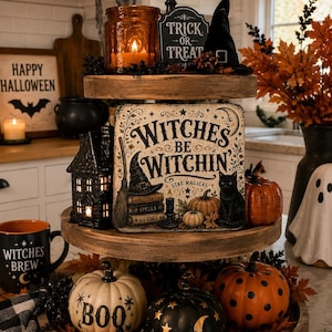 May include: A three-tiered wooden tray decorated for Halloween. The top tier holds an amber candle, a Trick or Treat sign, and a black witch hat. The middle tier features a sign reading Witches Be Witchin, a black house, and pumpkins. The bottom tier has three pumpkins with Boo, star, and polka dot patterns.