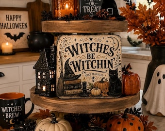 May include: A three-tiered wooden tray decorated for Halloween. The top tier holds an amber candle, a Trick or Treat sign, and a black witch hat. The middle tier features a sign reading Witches Be Witchin, a black house, and pumpkins. The bottom tier has three pumpkins with Boo, star, and polka dot patterns.