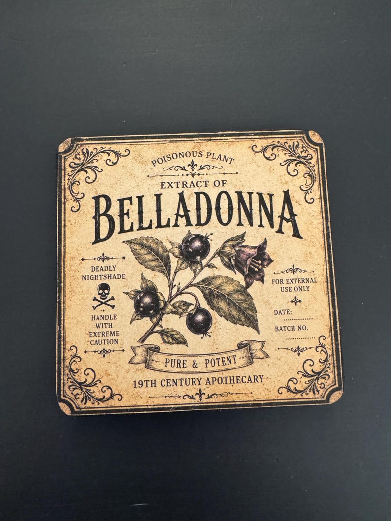 May include: A square coaster with a vintage-style beige label featuring the text "EXTRACT OF BELLADONNA" and "19TH CENTURY APOTHECARY." The design includes a botanical illustration of dark berries, a skull and crossbones icon, and decorative borders.