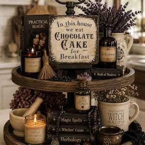 May include: A two-tiered wooden tray display featuring a sign that reads In this house we eat CHOCOLATE CAKE for Breakfast, alongside a Midnight Moon candle, a Belladonna bottle, a Book of Shadows, a Love Potion bottle, and a Vanilla Patchouli candle.