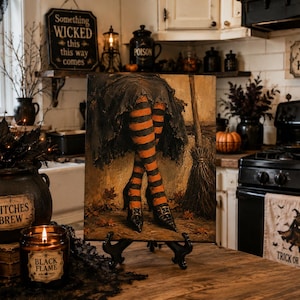 May include: A rectangular art print featuring a pair of legs wearing orange and black striped stockings and black pointed shoes, positioned beneath a dark skirt. The artwork includes a broomstick leaning against a wall and scattered autumn leaves.