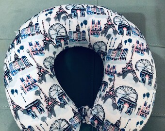May include: A white travel neck pillow with a print of Parisian landmarks, including the Eiffel Tower and the Ferris wheel.
