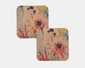 May include: Two square cork coasters with a floral design featuring pink and red cactus flowers, green leaves, and blue accents. The coasters have a light brown background.