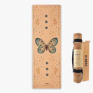 May include: A cork yoga mat featuring a butterfly design and a celestial pattern. The mat is rolled up and secured with a black strap. The mat is packaged in a brown cardboard box with the brand name "SCORIA" printed on it.