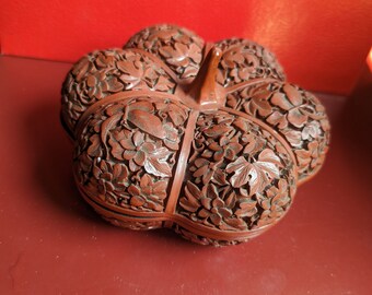 May include: A carved wooden container in the shape of a flower, with six sections. The container is a reddish-brown color and is intricately carved with floral and leaf patterns. The stem of the flower is visible at the top.