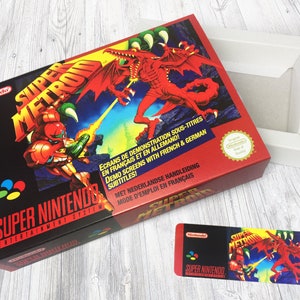 Peut inclure: Une boîte de cartouche de jeu Super Nintendo rouge et noire avec un dragon et un personnage en combinaison spatiale sur le devant. La boîte porte le texte "Super Metroid" et "Super Nintendo Entertainment System". La boîte est ouverte et l'intérieur est blanc.