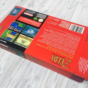 May include: A red and black Super Nintendo game box for The Legend of Zelda: A Link to the Past. The box features a picture of Link and the text "In an enchanted land. Imagine a land where reality and fantasy meet."