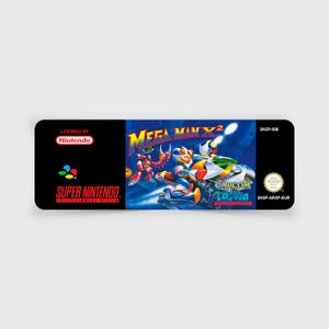 Peut inclure: Une cartouche de jeu Super Nintendo Entertainment System pour Mega Man X2, avec un fond bleu et noir représentant Mega Man X conduisant une moto. Le texte "Mega Man X2" est en blanc avec un "2" rouge. Le texte "SNSP-006" est en blanc sur fond noir dans le coin supérieur droit. Le texte "CAPCOM" est en blanc sur fond noir dans le coin inférieur droit. Le texte "LAGUNA" est en blanc sur fond noir sous "CAPCOM". Le texte "SNSP-ARXP-EUR" est en blanc sur fond noir dans le coin inférieur droit.