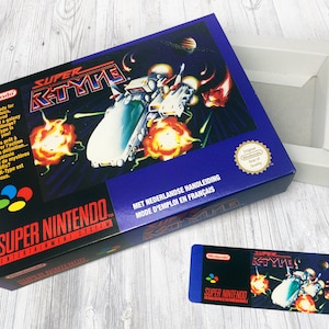 May include: A Super Nintendo Entertainment System game cartridge for Super R-Type. The box is purple with a picture of a spaceship shooting lasers. The text on the box says "Super R-Type" and "Super Nintendo Entertainment System".