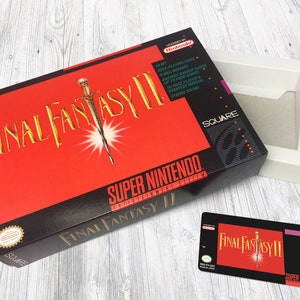 Puede incluir: Una caja de juego de Super Nintendo roja y negra para Final Fantasy II. La caja presenta una espada dorada y el texto "Final Fantasy II" en fuente dorada. La caja está abierta y el cartucho del juego es visible. El cartucho es negro con una etiqueta roja y dorada que dice "Final Fantasy II" y tiene una imagen de una espada.