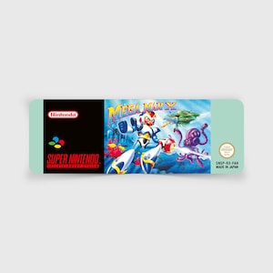Könnte beinhalten: Eine Super Nintendo Videospielkassette für Mega Man X. Das Box-Art zeigt einen futuristischen Robotercharakter in einem blau-weißen Anzug, der gegen Feinde kämpft. Die Kassette hat einen schwarzen Rücken mit den Nintendo- und Super Nintendo-Logos.