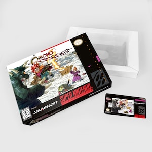 Peut inclure: Une boîte de cartouche de jeu Super Nintendo noire et blanche avec une illustration colorée de personnages du jeu Chrono Trigger. La boîte est ouverte et la cartouche de jeu est visible à l'intérieur. La cartouche de jeu est noire avec une illustration colorée de personnages du jeu.