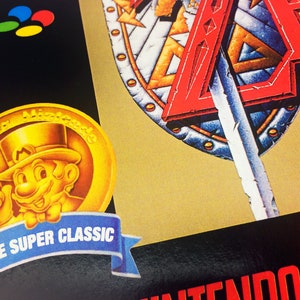 May include: A gold coin featuring a cartoon character wearing a top hat and a moustache. The coin has the text "Super Nintendo" around the edge. The coin is on a blue ribbon with the text "S&eacute;rie Super Classic".