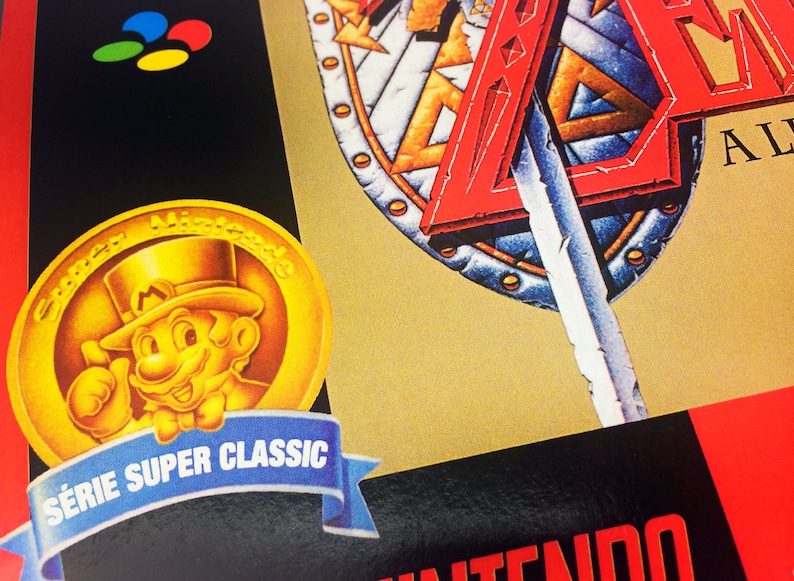 May include: A gold coin featuring a cartoon character wearing a top hat and a moustache. The coin has the text "Super Nintendo" around the edge. The coin is on a blue ribbon with the text "S&eacute;rie Super Classic".