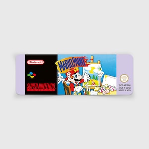 Puede incluir: Un cartucho de juego de Super Nintendo para Mario Paint. El cartucho tiene un borde púrpura y presenta el logotipo de Nintendo, el logotipo de Super Nintendo y el título de Mario Paint con Mario haciendo una señal de aprobación.