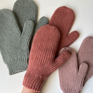 Könnte beinhalten: Drei Paar Strickhandschuhe in verschiedenen Farben: Grau, Rosa und Rotbraun. Die Handschuhe sind mit einer einfachen Strickmasche gearbeitet und haben ein Daumenloch.