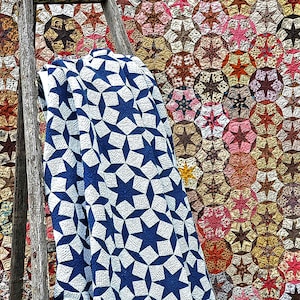 May include: A blue and white quilt with a star pattern is draped over a wooden ladder. The quilt is leaning against a colorful patchwork quilt with a star pattern.