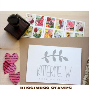 May include: A white card with a grey branch design and the text "KATERINE. W WEDDING DESIGN" printed on it. The card is sitting on a brown surface with a wooden stamp and a row of vintage postage stamps.