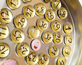 May include: A set of gold-colored round magnets with black numbers 1 through 31. The magnets are arranged in a spiral pattern inside a silver metal container. Two small magnets with cupcake designs are in the center of the container.