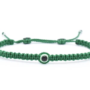 May include: A green string bracelet with a black evil eye charm. The bracelet is tied with a knot and has a sliding knot for adjusting the size.