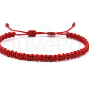 May include: A red macrame bracelet with an adjustable sliding knot closure. The bracelet is made of woven red cord and is displayed against a white background. The bracelet is a simple, minimalist design.
