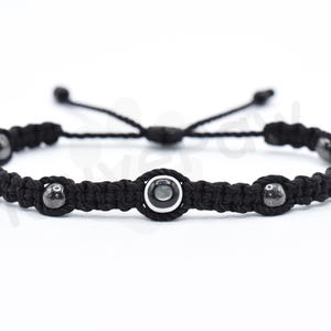 May include: Black braided bracelet with three black beads and a silver bead with a black center.