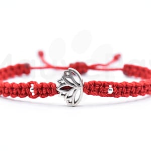 May include: Red string bracelet with a silver lotus charm. The bracelet is made of braided string and has silver beads.