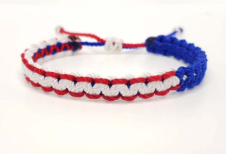 May include: A red, white, and blue braided friendship bracelet. The bracelet is made with a knotting technique and has a simple design.