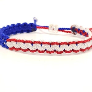 May include: A blue, white, and red braided friendship bracelet. The bracelet is made with a knotting technique that creates a striped pattern.