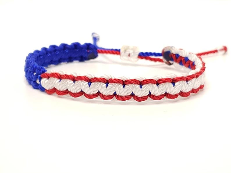 May include: A blue, white, and red braided friendship bracelet. The bracelet is made with a knotting technique that creates a striped pattern.