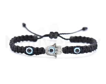 May include: Black macrame bracelet featuring a silver Hamsa hand charm and two blue evil eye beads. The bracelet is adjustable with a sliding knot closure. A stylish accessory for everyday wear.