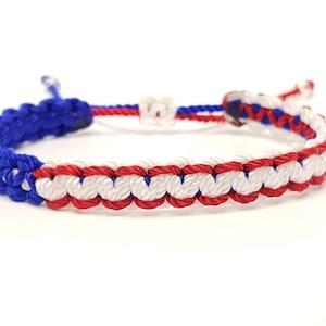 May include: A blue, white, and red braided friendship bracelet. The bracelet is made of woven string and has a simple knot closure.