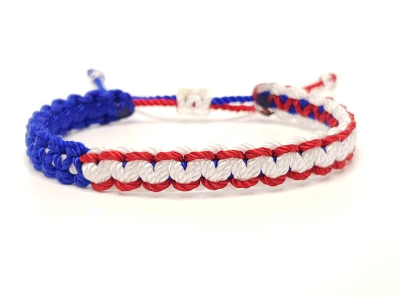 May include: A blue, white, and red braided friendship bracelet. The bracelet is made of woven string and has a simple knot closure.