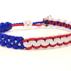 May include: A blue, white, and red braided friendship bracelet. The bracelet is made of three different colors of string that are woven together in a pattern.