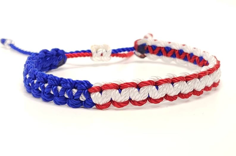 May include: A blue, white, and red braided friendship bracelet. The bracelet is made of three different colors of string that are woven together in a pattern.