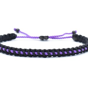 May include: A black and purple macrame bracelet. The bracelet features a woven design with black and purple threads. The adjustable closure is purple. This handmade bracelet is a stylish accessory.