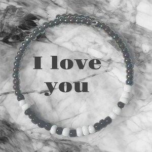 May include: A black and white beaded bracelet with iridescent beads. The bracelet has the words "I love you" written on a white background.