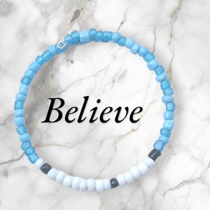 May include: A blue and white beaded bracelet with the word "Believe" in black lettering.